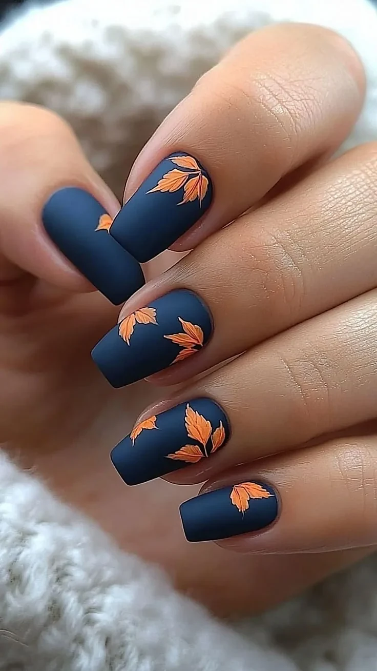Short square nails in matte navy blue with orange maple leaves